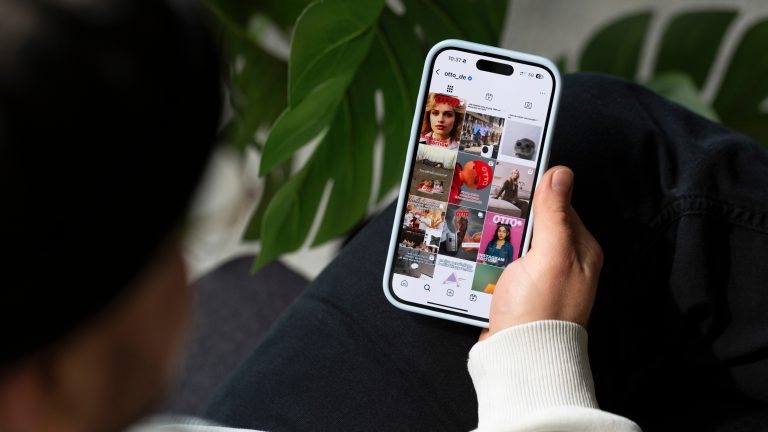 Der Blick über die Schulter einer Person auf ein Handy auf ihrem Bein, das den Instagramfeed von Otto.de zeigt.