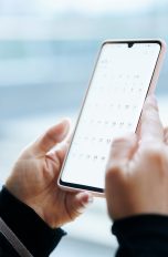 Kalender Apps im Vergleich, So organisierst du deinen Alltag digital Nahaufnahme von zwei Händen, die ein Smartphone halten. Auf dem Screen erscheint eine geöffnete Kalender-App.