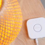 Eine Philips-Hue-Bridge liegt neben einer eingeschalteten Lampe auf einem Tisch.