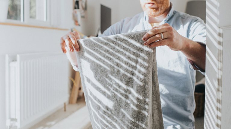 Neue Energieeffizienzklassen beim Trockner, Das musst du wissen Eine Person steht in einem hellen Raum und faltet ein frisch gewaschenes Handtuch.