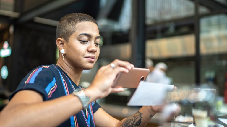 Eine Person sitzt in einem öffentlichen Raum und hält ihr Smartphone über eine Visitenkarte, um diese zu scannen.