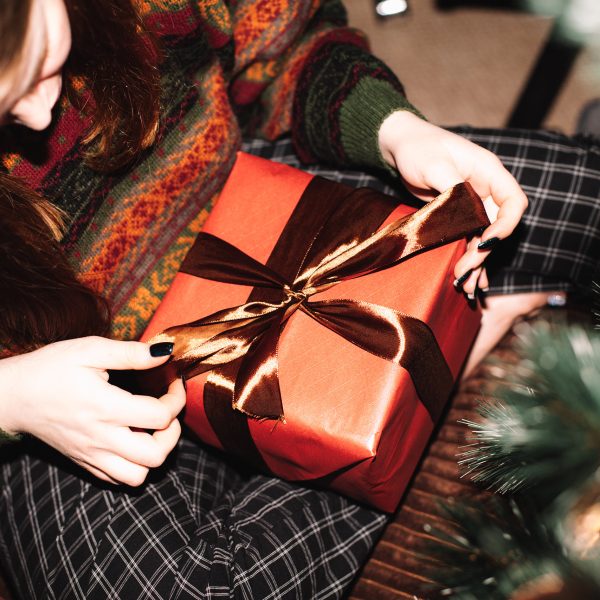 Vogelperspektive auf eine Person, die vor einem Weihnachtsbaum sitzt und ein Geschenk auf ihrem Schoß hat.