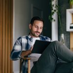 Eine Person sitzt mit überschlagenen Beinen auf einem Stuhl. Auf dem Schoß hält sie ein iPad.