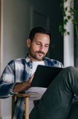 Eine Person sitzt mit überschlagenen Beinen auf einem Stuhl. Auf dem Schoß hält sie ein iPad.
