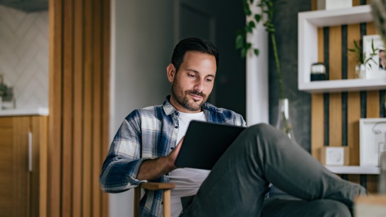 Eine Person sitzt mit überschlagenen Beinen auf einem Stuhl. Auf dem Schoß hält sie ein iPad.