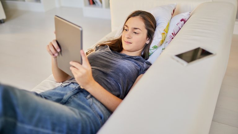 WhatsApp & iPad, So klappt es mit der Kombination Eine Person liegt auf einem Sofa und hält ein iPad in den Händen.